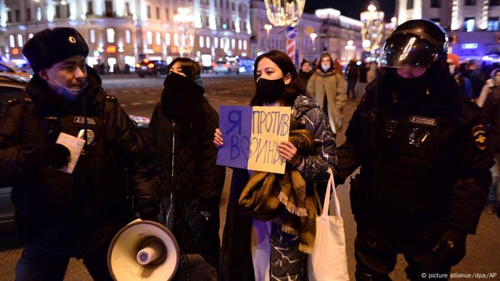 Young female anti-war protester holding a sign and being escorted by two police officers