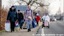 BEREGSURANY, HUNGARY - FEBRUARY 25: People walk with their belongings at the Astely-Beregsurany border crossing as they flee Ukraine on February 25, 2022 in Beregsurany, Hungary. Long queues have already formed at the Hungarian-Ukrainian border crossings after Russia began a large-scale attack on Ukraine in the early hours of February 24, with explosions reported in multiple cities and far outside the restive eastern regions held by Russian-backed rebels. (Photo by Janos Kummer/Getty Images)