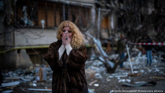 A woman stands outside her badly damaged home after a rocket attack in Kyiv