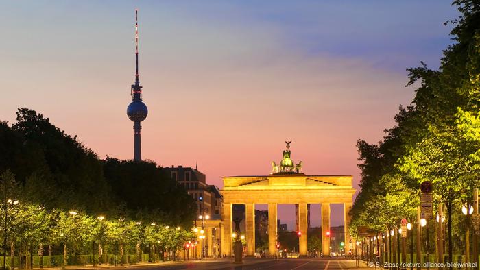 La Puerta de Brandeburgo de Berlín iluminada de noche con la puesta de sol detrás.