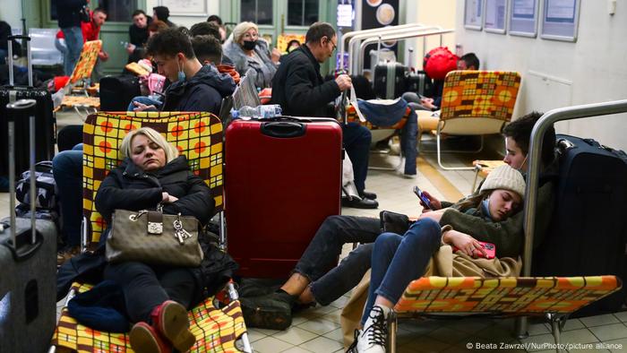 Passengers rest on camp beds in a temporary shelter inside a building