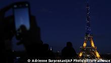 People photograph the Eiffel Tower, lighted with the colors of Ukraine, Friday, Feb.25, 2022 in Paris. Russian troops bore down on Ukraine's capital Friday, with gunfire and explosions resonating ever closer to the government quarter, in an invasion of a democratic country that has fueled fears of wider war in Europe and triggered worldwide efforts to make Russia stop. (AP Photo/Adrienne Surprenant)