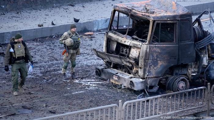 Two Ukrainian soldiers inspecting a destroyed truck in Kyiv on February 26