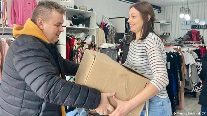 Eine Frau gibt einem Mann einen Karton in einem Geschäft mit Kleidern