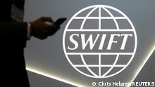 FILE PHOTO: A man using a mobile phone passes the logo of global secure financial messaging services cooperative SWIFT at the SIBOS banking and financial conference in Toronto, Ontario, Canada October 19, 2017. REUTERS/Chris Helgren/File Photo