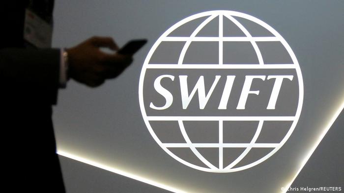 A person holding a mobile phone next to the SWIFT payment logo
