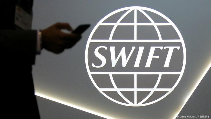 A person holding a mobile phone next to the SWIFT payment logo