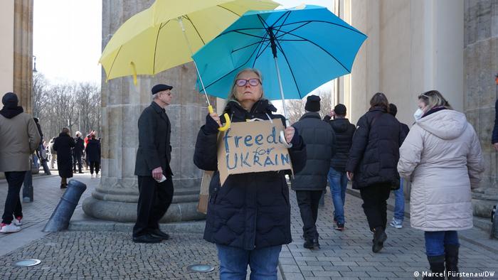 Woman holds a green and a yellow umbrella and a sign that reads Freedom For Ukraine