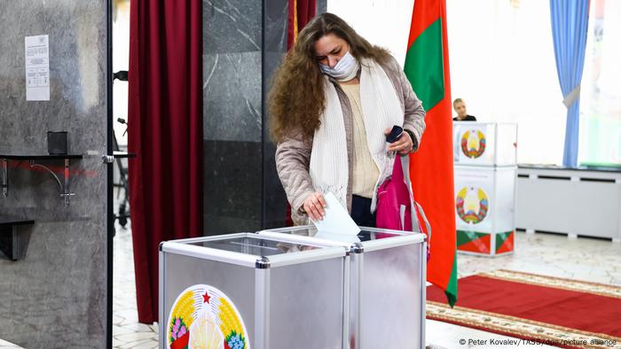 A woman diposits a ballot into an urn with the Belarusian coat of arms on it A woman diposits a ballot into an urn with the Belarusian coat of arms on it