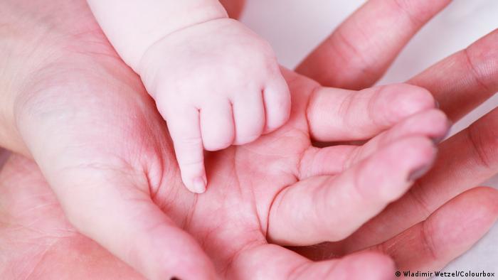 A baby's hand rests on its mother's hand
