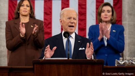 Biden fala em um púlpito. Atrás, Kamla Harris e Nancy Pelosi aplaudem