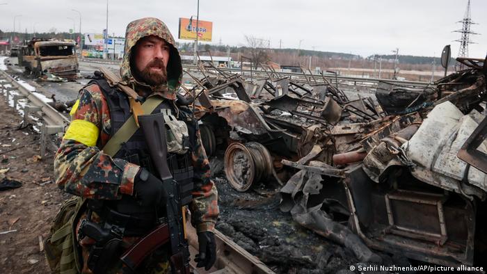 An armed man stands by the remains of a Russian military vehicle in Bucha, close to the capital Kyiv