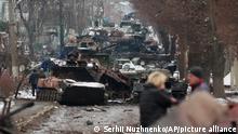 People look at the gutted remains of Russian military vehicles on a road in the town of Bucha, close to the capital Kyiv, Ukraine, Tuesday, March 1, 2022. (AP Photo/Serhii Nuzhnenko)