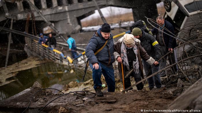 زنی اوکراینی به کمک دو نفر از پلی ویران می‌گذرد