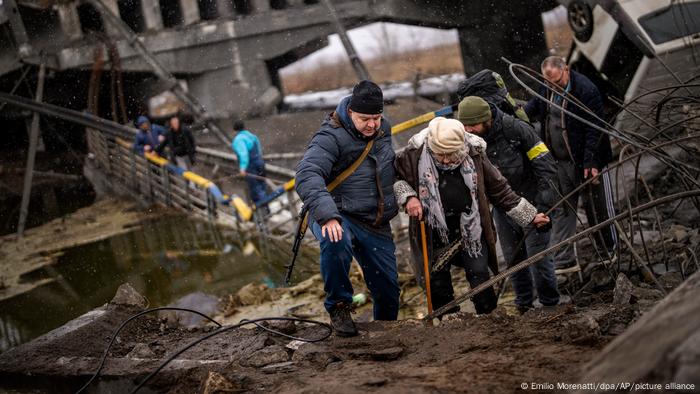Başkent Kiev'de, Rus topçu ateşi sonucu yıkılan bir köprünün üzerinden geçmeye çalışan yaşlı bir kadın ve ona yardım edenler
