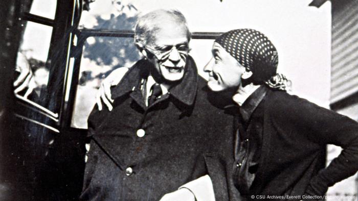 Alfred Stieglitz und Georgia O'Keeffe lächeln sich in einem Schwarz-weiß-Bild an, sie hat ihren Arm um die Schultern ihres Partners gelegt.