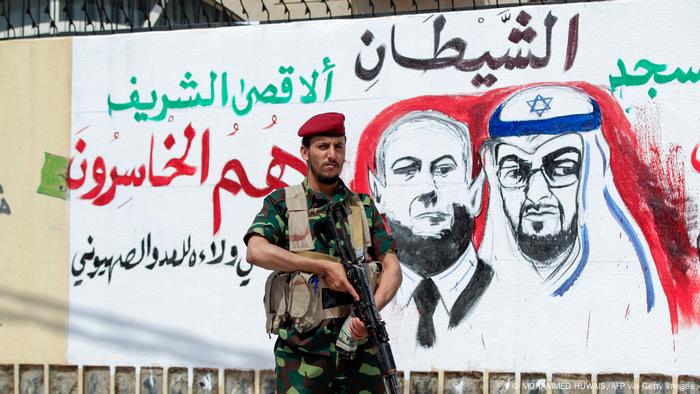 A fighter loyal to Yemen's Huthi rebels stands guard next to a mural denouncing Abu Dhabi Crown Prince Sheikh Mohammed bin Zayed Al Nahyan (R) and Israeli Prime Minister Benjamin Netanyahu, during a rally in the capital Sanaa.