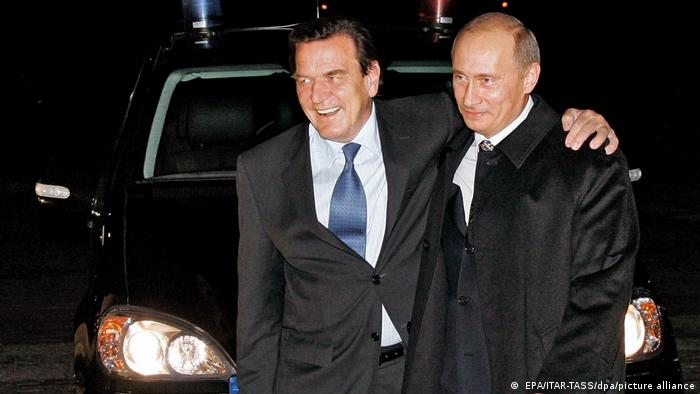 Gerhard Schröder and Vladimir Putin stand side by side in front of a car