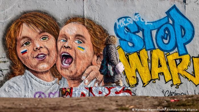 A graffiti mural shows two girls, one with the Russian flag on her face and the other with the Ukrainian flag, hugging each other with the words Stop War next to them.