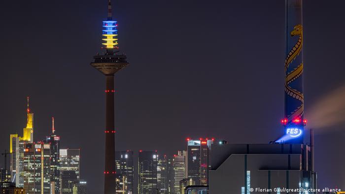 The Frankfurt TV tower is lit up at night in yellow and blue.
