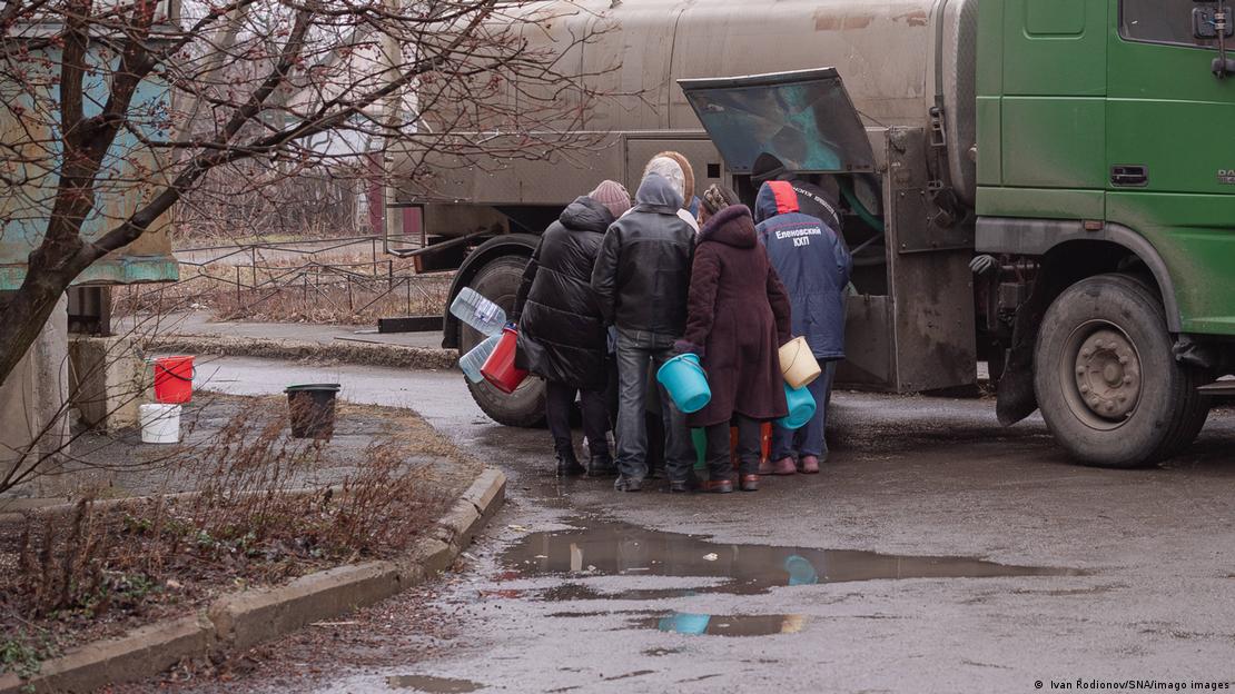 Indivíduos reunidos ao lado de caminhão de entrega de água