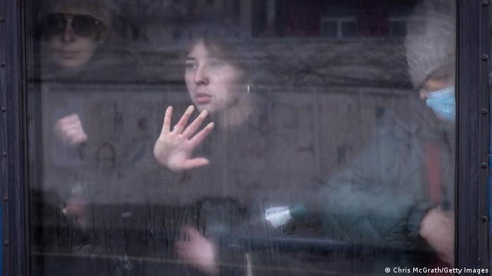 Faces of three people behind a train window, one places hand on glass