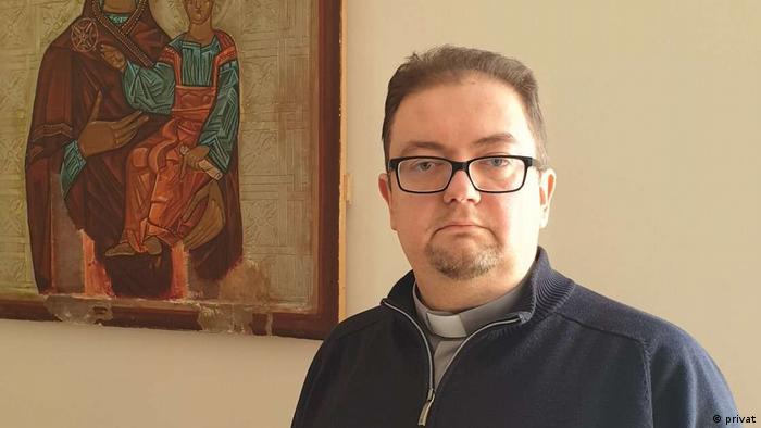 Andriy Dmytryk wears glass and has a goatee, a zip-up sweater over a grey shirt, collar