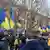 A group of people gather in a city street, holding Ukrainian flags