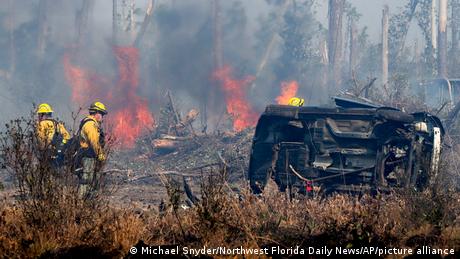 Two firefighters near a burnt-out car