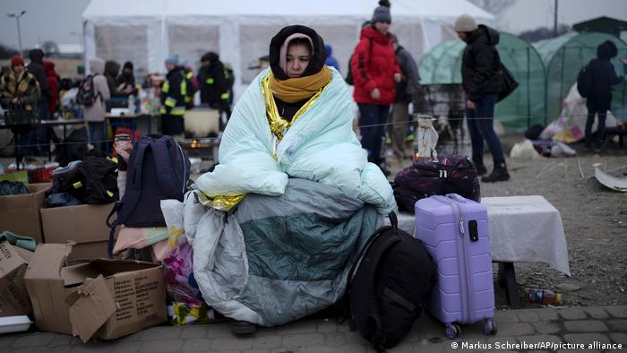 A woman wrapped up in a blanket sits with her luggage at Poland's Medyka border crossing