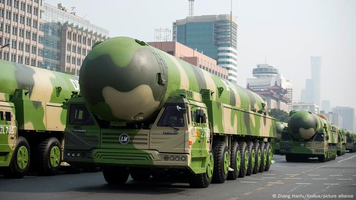 Lastwagen mit riesigen Raketen in Tarnanstrich paradieren durch eine Stadt mit Hochhäusern