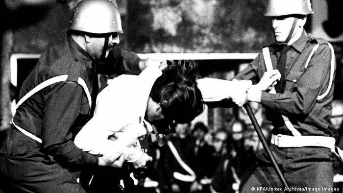 Film still from 'Z': A black-and-white photo of a man being violently arrested.