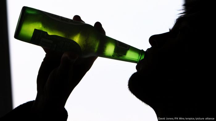 Profilansicht eines Mannes, der aus einer Bierflasche trinkt.