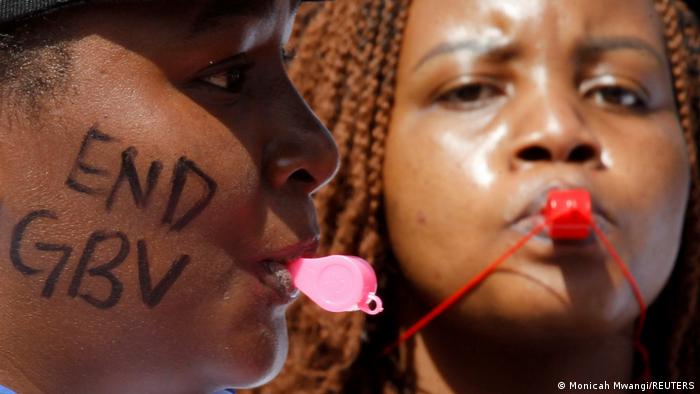 Nahaufnahme zweier schwarzer Frauen mit Trillerpfeifen. Auf einer Wange die Aufschrift End GBV (gender-based violence) 