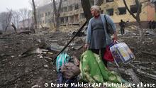 09.03.2022 *** Eine Frau steht mit ihrem Gepäck vor einer durch einen Angriff beschädigten Geburtsklinik in Mariupol. +++ dpa-Bildfunk +++