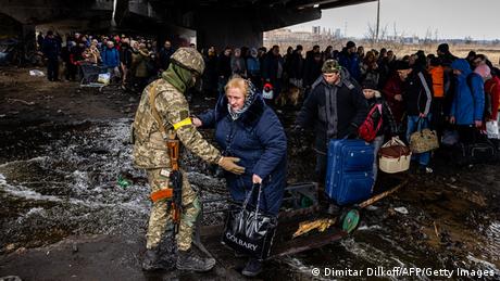 Un soldado ucraniano ayuda a una mujer mayor a cruzar un puente destruido en Irpin.