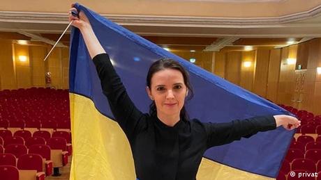 Dirigentin Oksana Lyniv mit ukrainischer Flagge in einem leeren Konzertsaal.