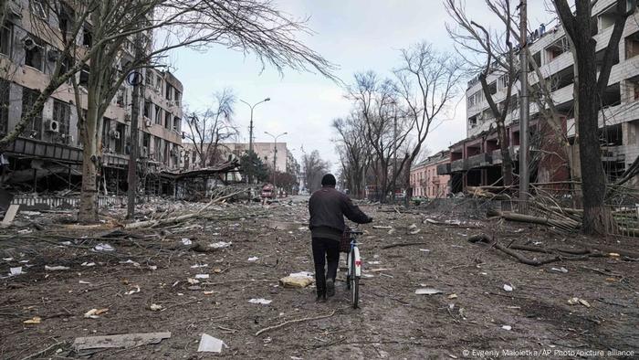 A man walks a bike through debris in Mariupol