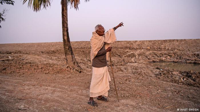 A man stands in an arid landscape and points in the distance 