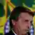 Foto do rosto de Bolsonaro. Ele fala ao microfone, sério.