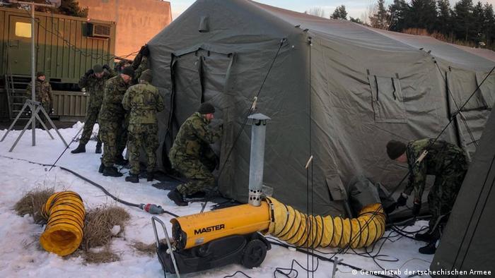 Soldiers outdoors, snow on the ground, working on setting up tents 