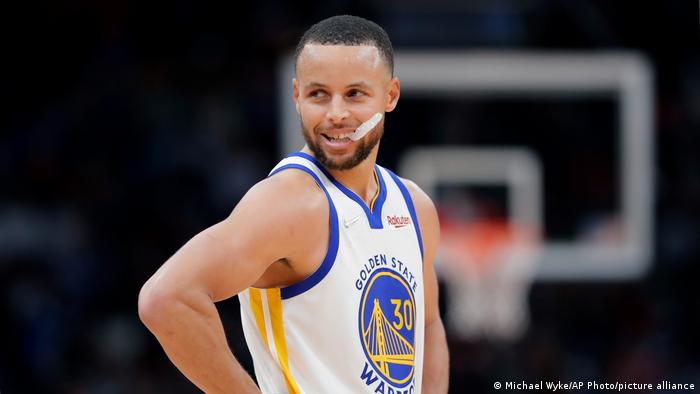 Basketball-Profi Stephen Curry schaut während einer Spielpause lächelnd über die Schulter und kaut auf seinem Zahnschutz