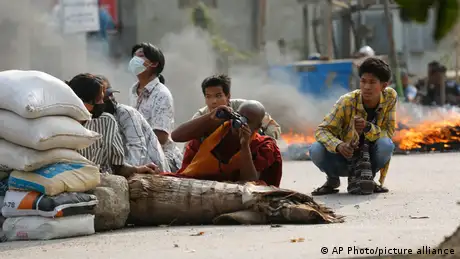 A Buddhist monk uses binoculars while with other men squatting behind a road barricade in Mandalay, Myanmar.