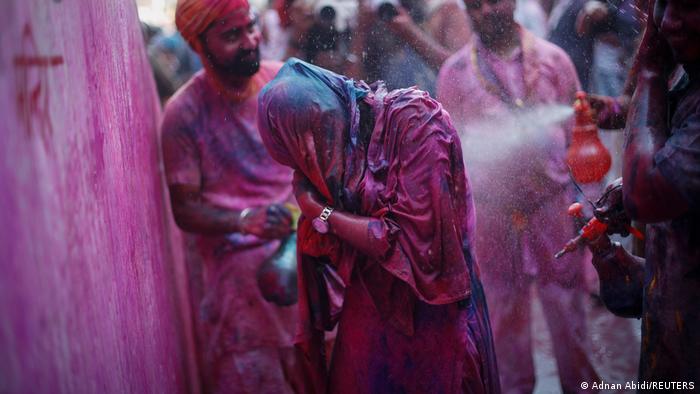 Ein Frau wird während des Lathmar Holi 2022 mit farbigem Wasser bespritzt.