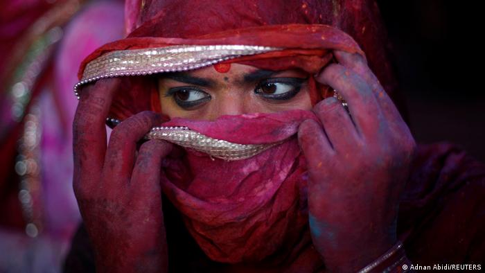 Eine Frau richtet während des Lathmar Holi 2022 ihren Schal um ihre Augen vor dem Farbpulver zu schützen.