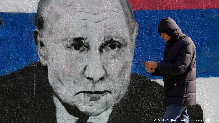 A man walks past a mural of Putin