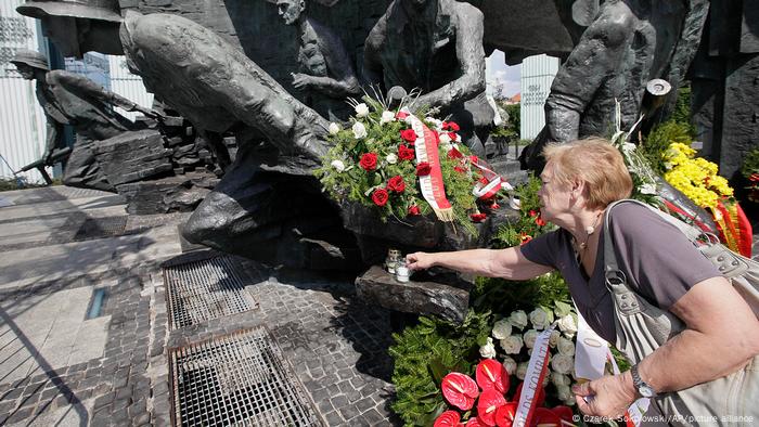 Femme allumant des bougies à un monument commémorant l'Insurrection de Varsovie