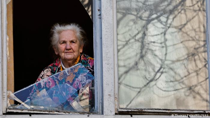 Ukraine | Bewohnerin schaut aus einem beschädigten Hasu nach Luftangriffen in Kiew