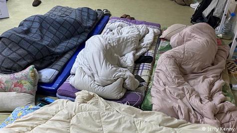 Pessoas cobertas dormindo em colch&otilde;es no ch&atilde;o