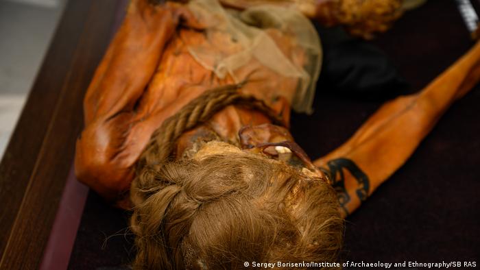 A mummified body, hair in braids and a tattooed arm.